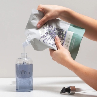 Mãos despejando líquido azul de embalagem flexível branca e verde para garrafa transparente com texto CASTELBEL