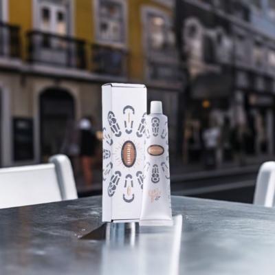 Tubo e caixa de creme de barbear branco sobre mesa metálica com cadeiras ao fundo.