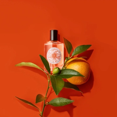 Frasco de perfume com ramo de laranja e fruta laranja ao lado num fundo laranja