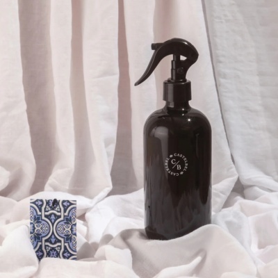 Frasco preto de spray sobre tecido branco com padrão azul e branco ao lado
