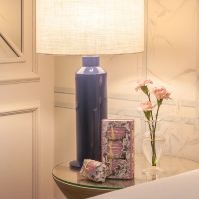 Mesa com lâmpada azul, sabonetes embalados e vaso com flores cor-de-rosa
