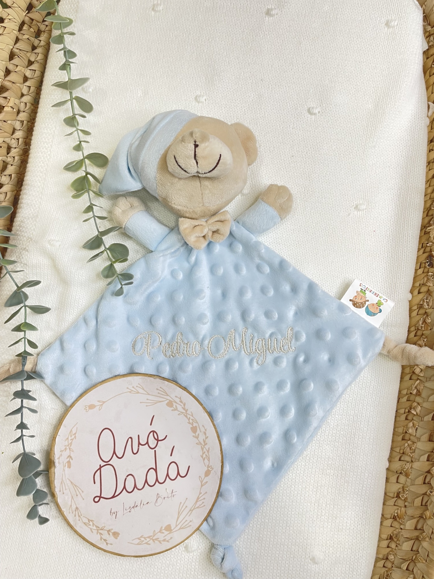 Boneco de peluche azul com manta branca e cartão decorativo redondo