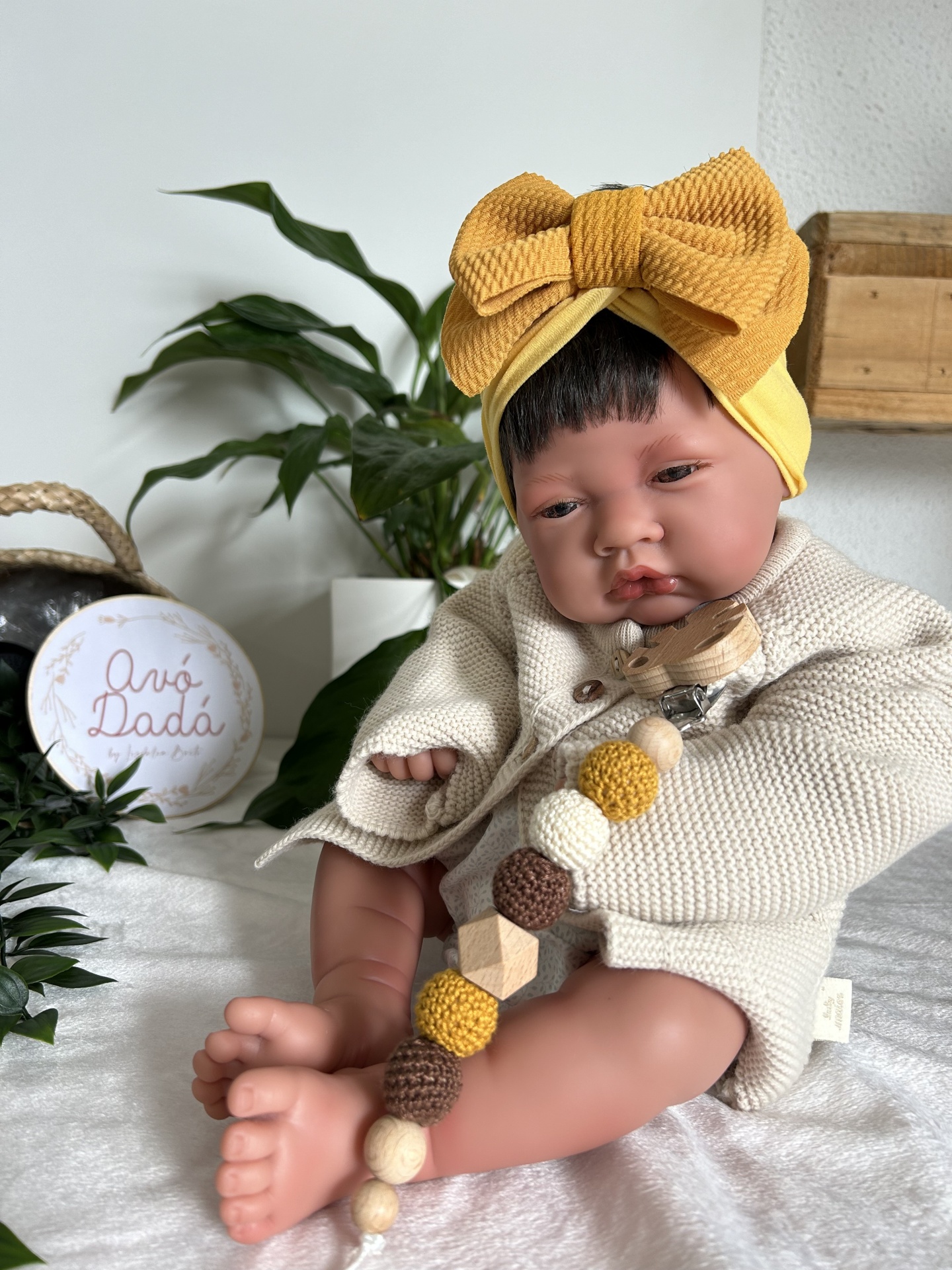 Boneca realista com camisola cremosa e faixa de cabeça amarela com laço