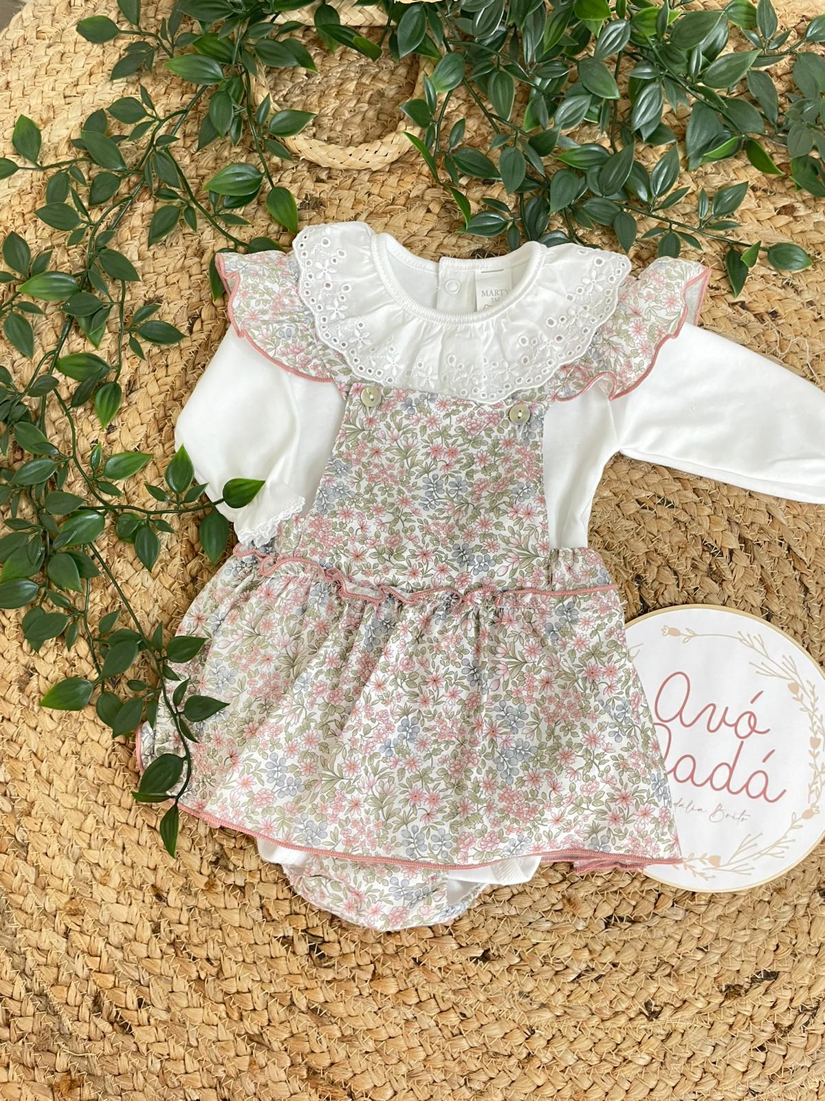 Conjunto de roupa para bebé com body branco e vestido floral rosa e verde sobre tapete natural