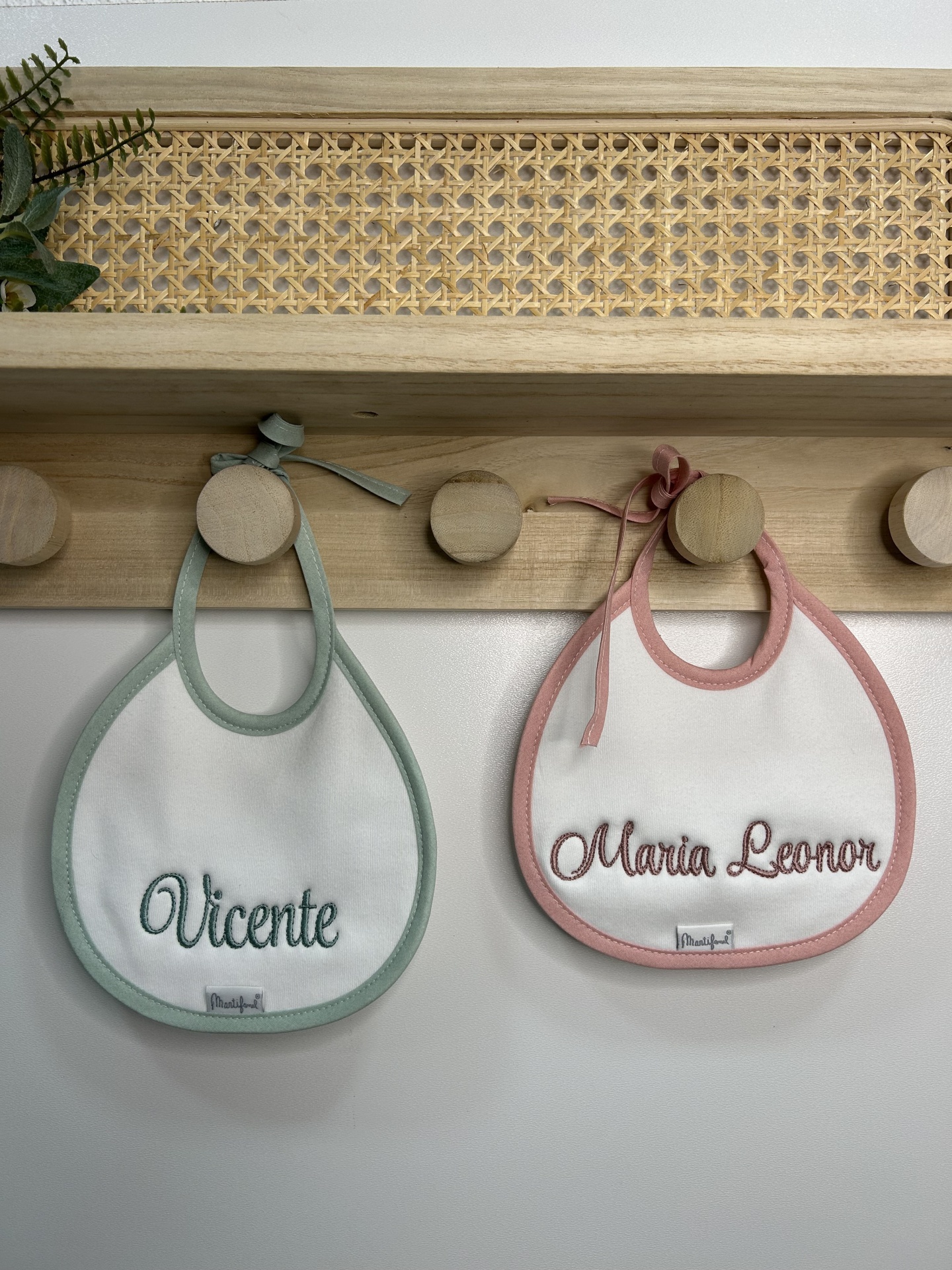Dois babetes de bebé com nomes bordados pendurados em ganchos de madeira