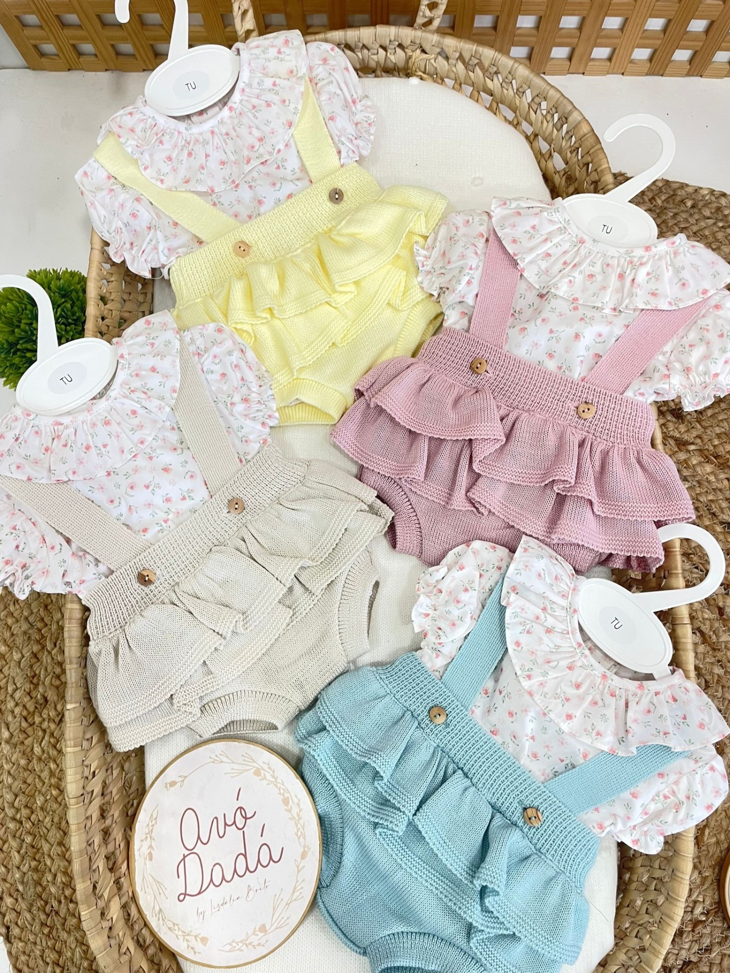 Conjunto de roupa para bebé com blusa floral e jardineira de malha colorida num berço de vime.
