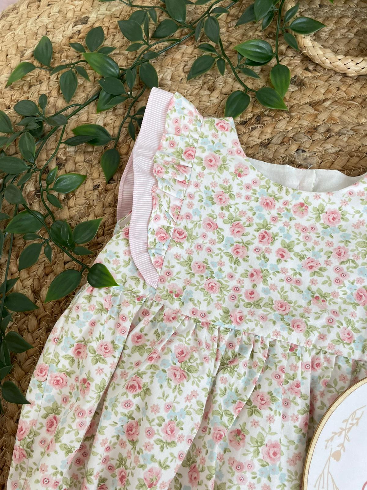 Vestido infantil floral branco com detalhes rosa sobre tapete de fibra natural