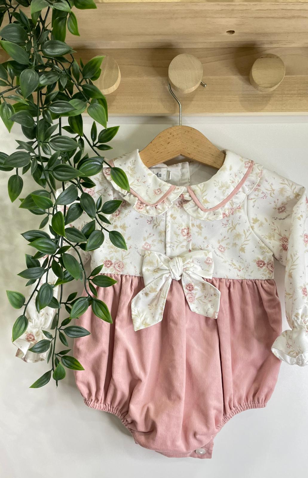 Body de bebé branco com padrão floral rosa e bege e parte inferior rosa claro pendurado em cabide de madeira