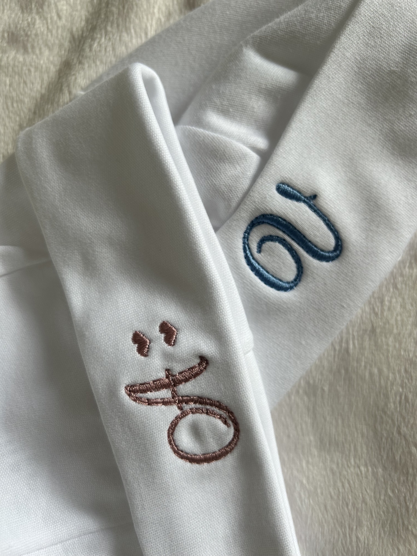 Tecido branco com bordados em azul e cor de rosa sobre uma superfície peluda clara