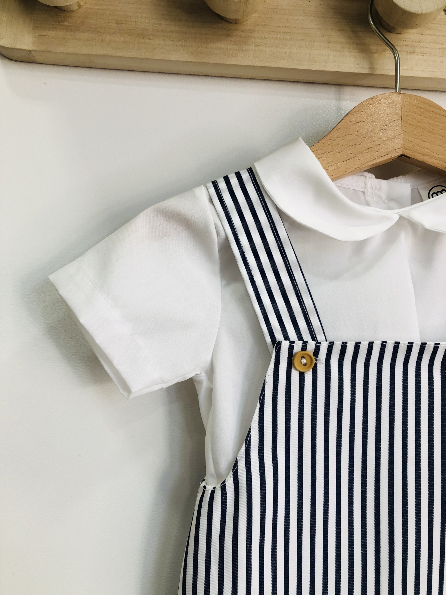 Roupa de bebé branca com macacão riscado azul e branco pendurada num cabide de madeira