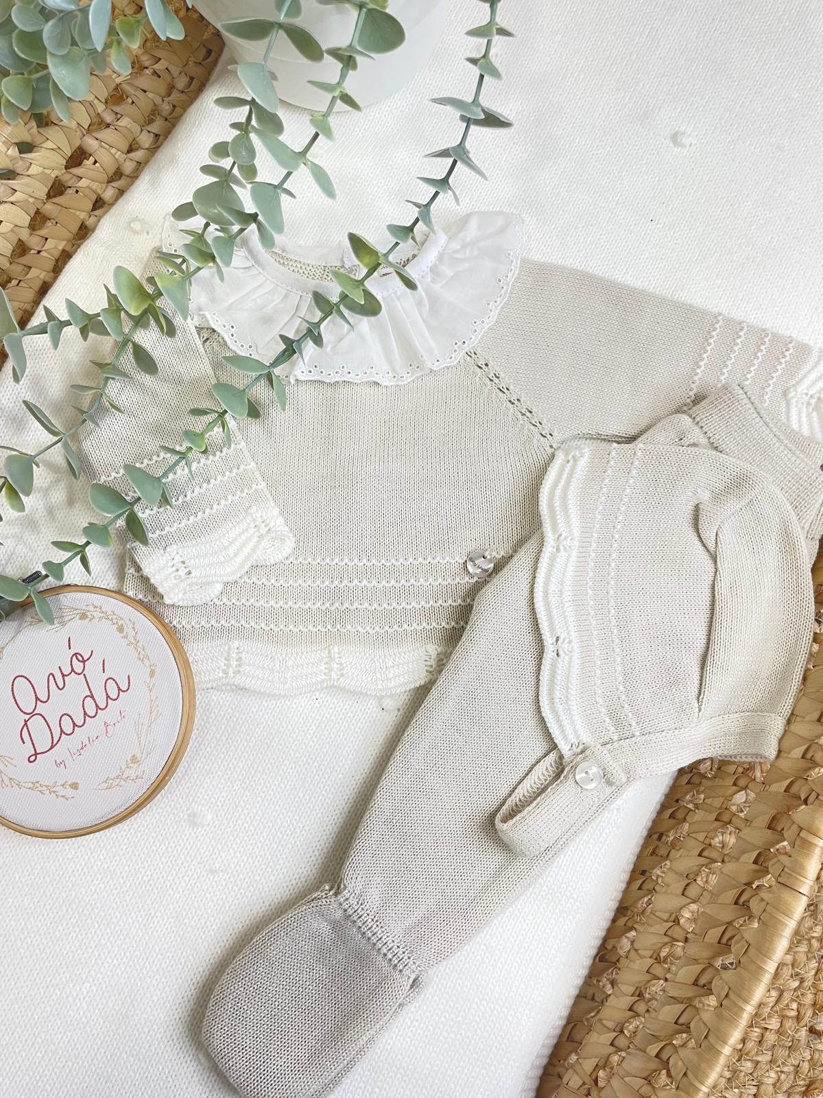 Conjunto de roupa de bebé bege e branco em malha com gola e botões, sobre tapete de palha e fundo branco