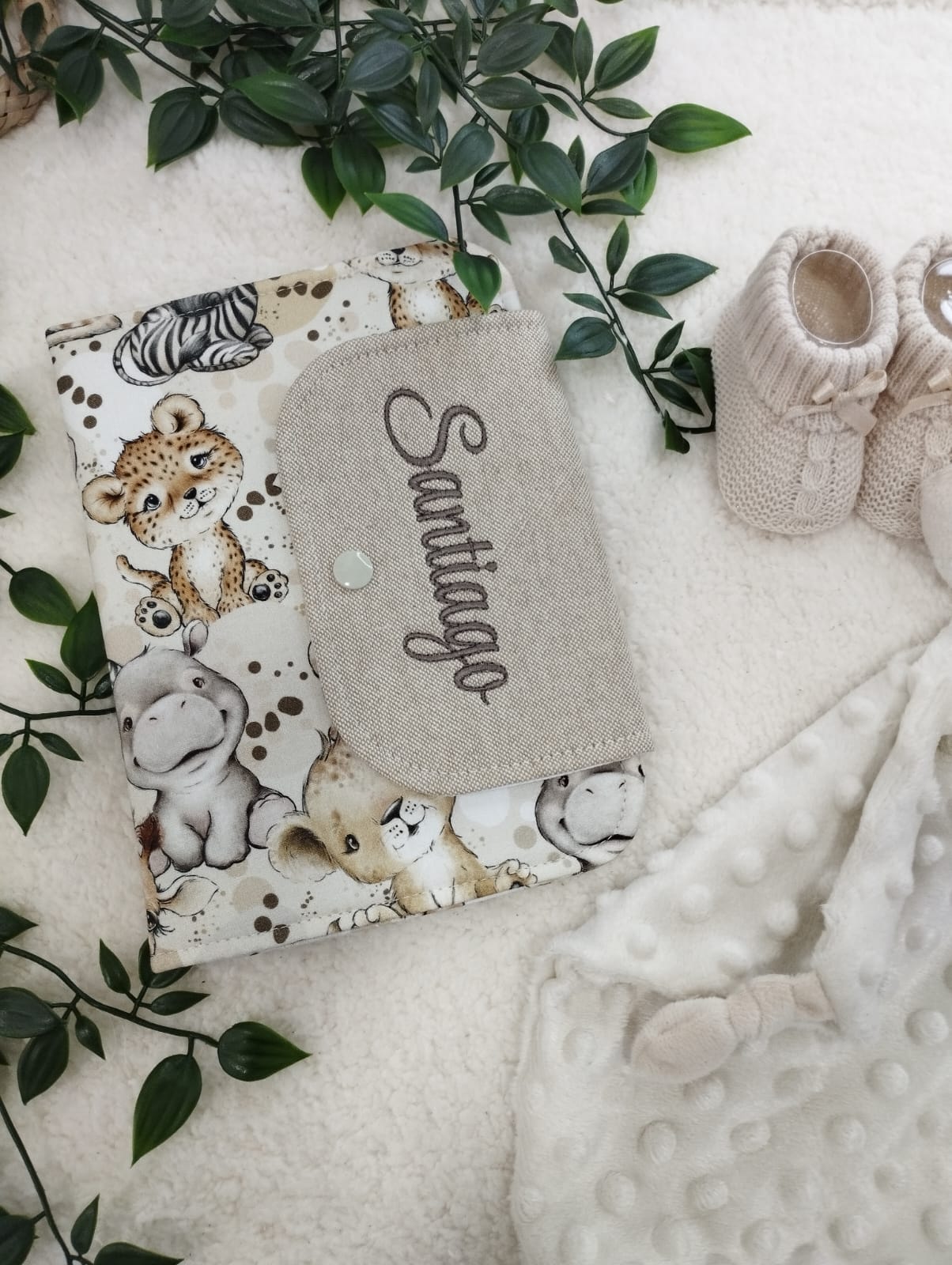 Capa para caderno com estampa de animais selvagens e nome bordado Santiago, com sapatinhos e manta ao lado