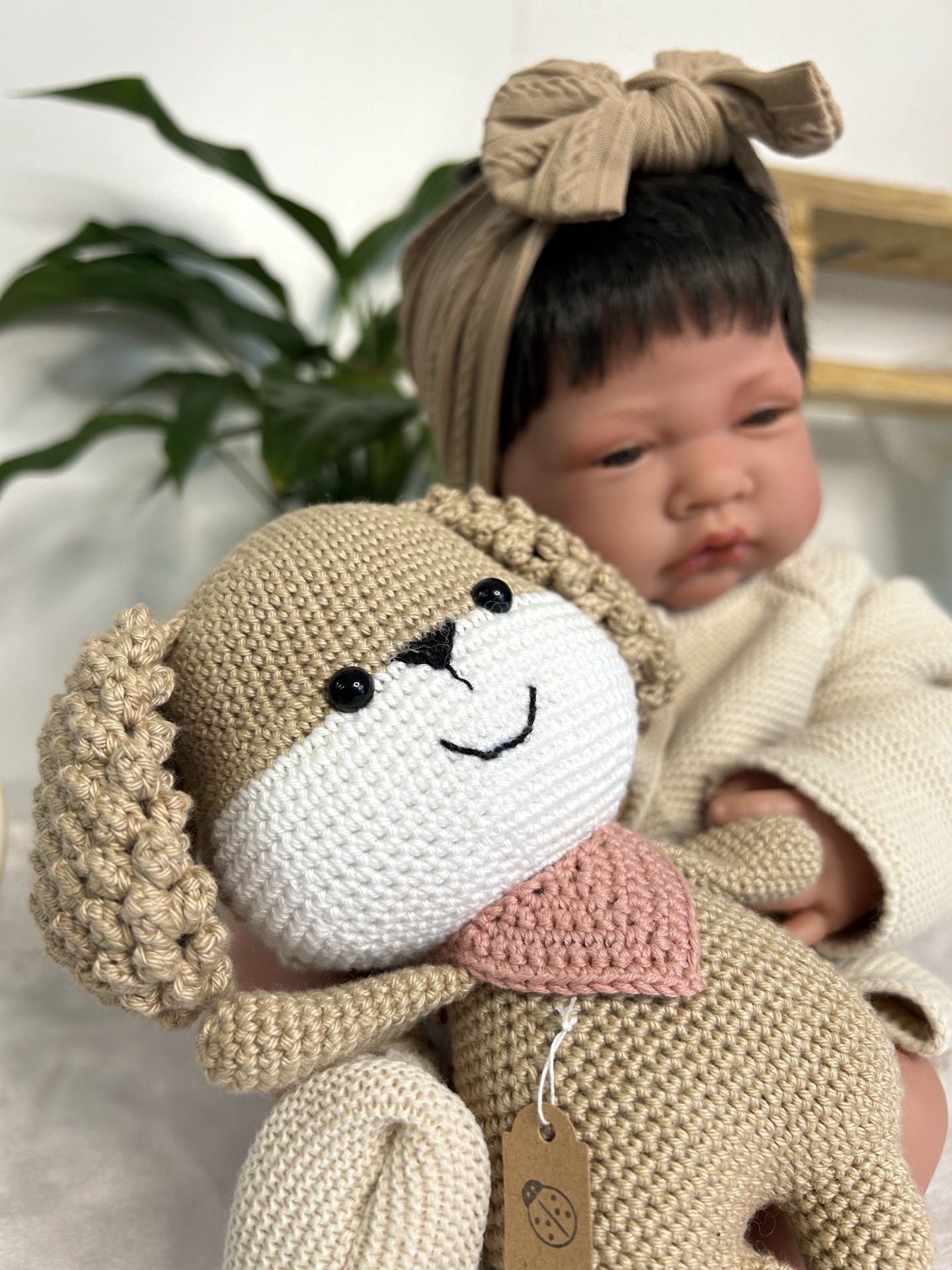 Bebé com boneco cão em crochet beige sentado, com planta verde e prateleira de madeira