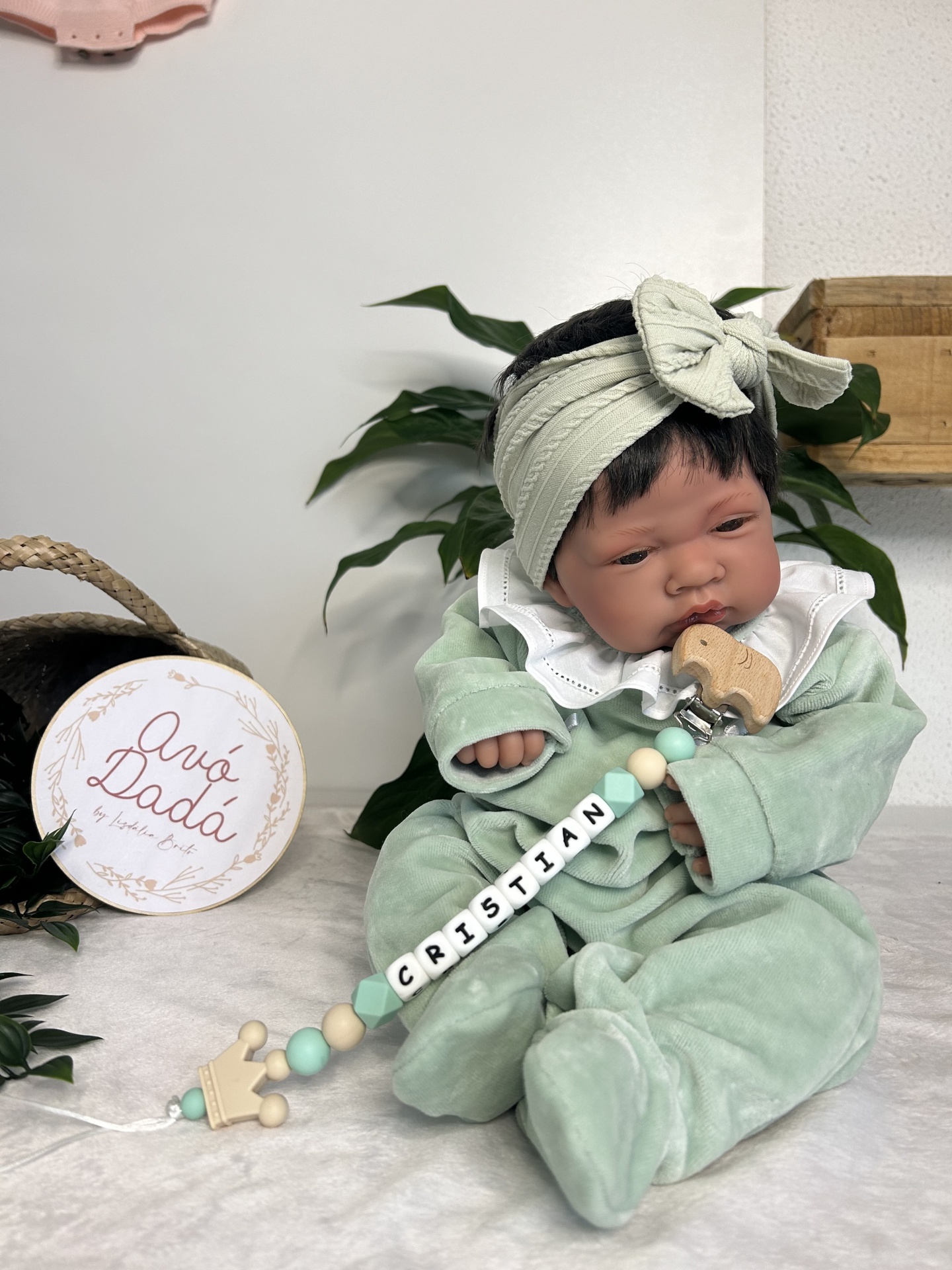 Boneco bebé com roupa verde e prendedor de chupeta personalizado.