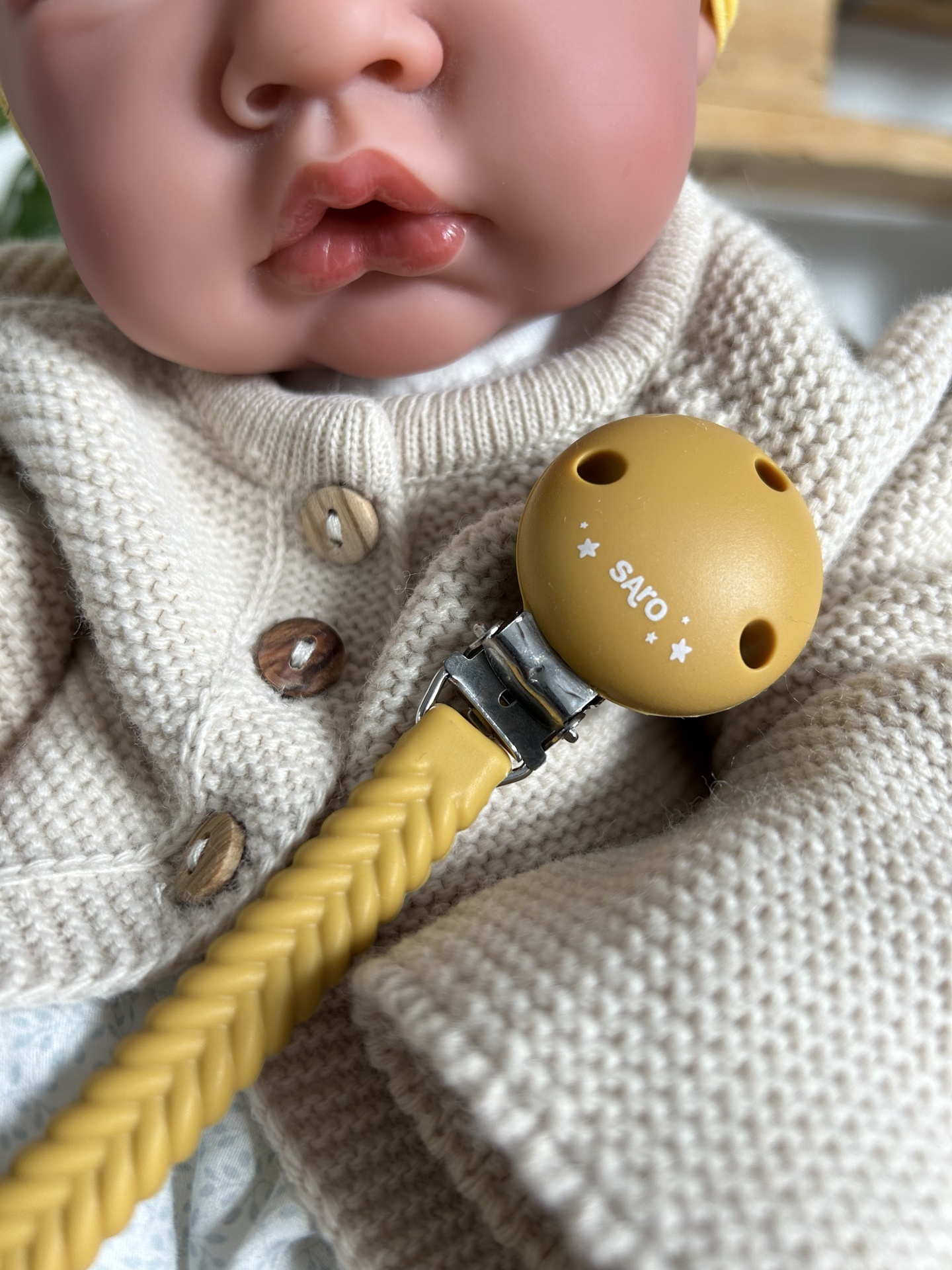 Chupeta amarela com clip e cordão sobre roupa creme de boneca realista