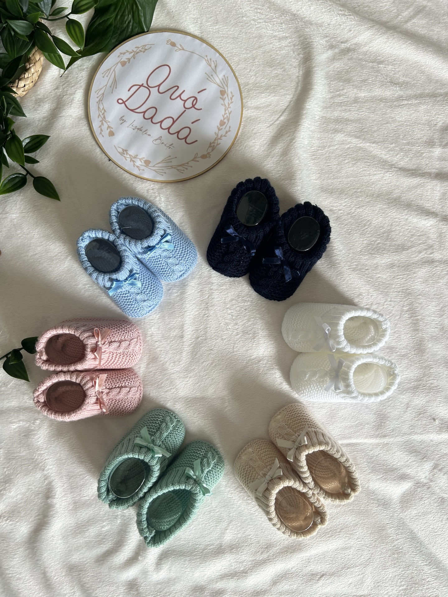 Sapatinhos de bebé tricotados coloridos sobre tecido branco com placa 'Avó Dadá'