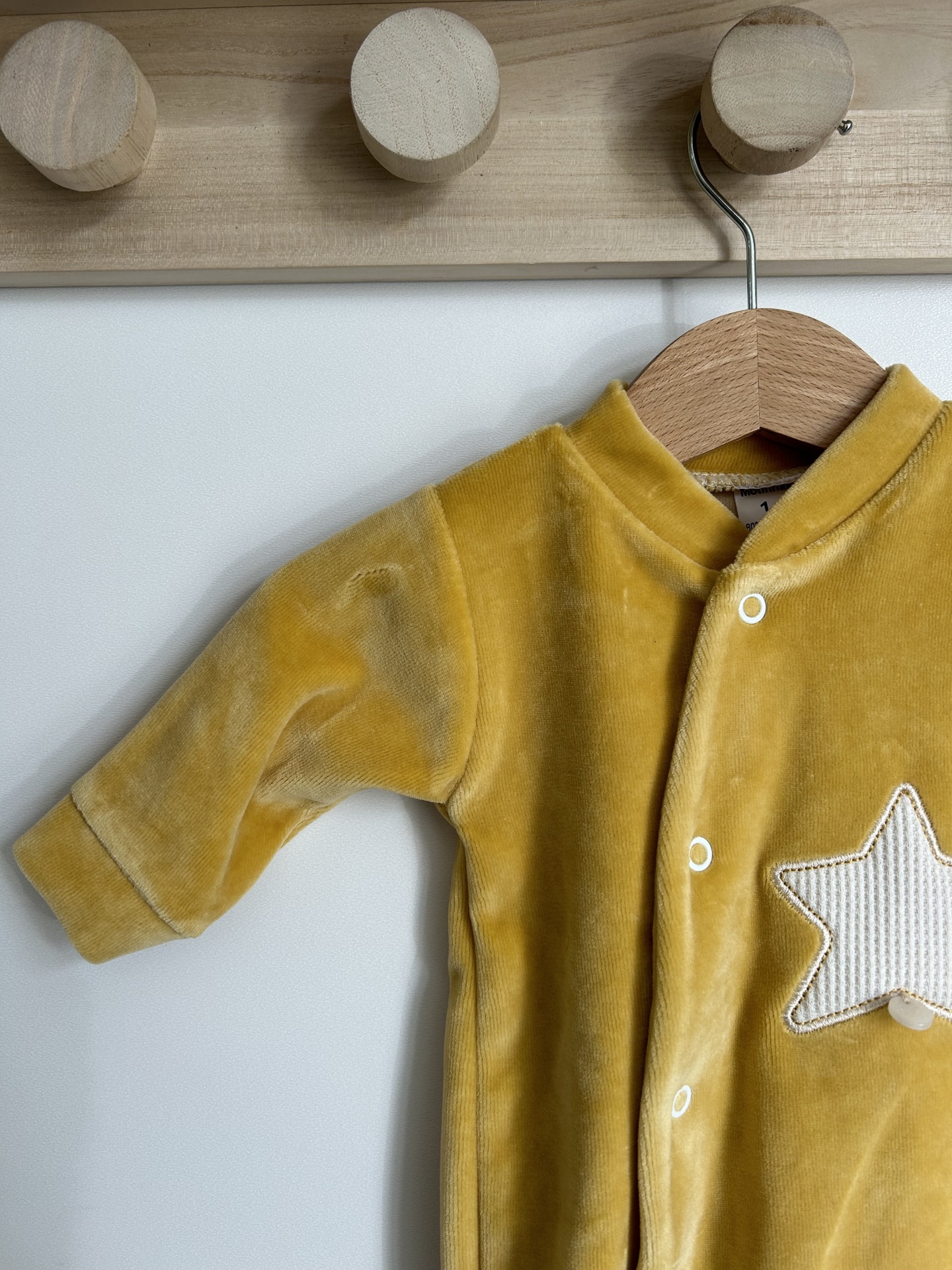 Macacão de bebé amarelo com estrela branca pendurado num cabide de madeira