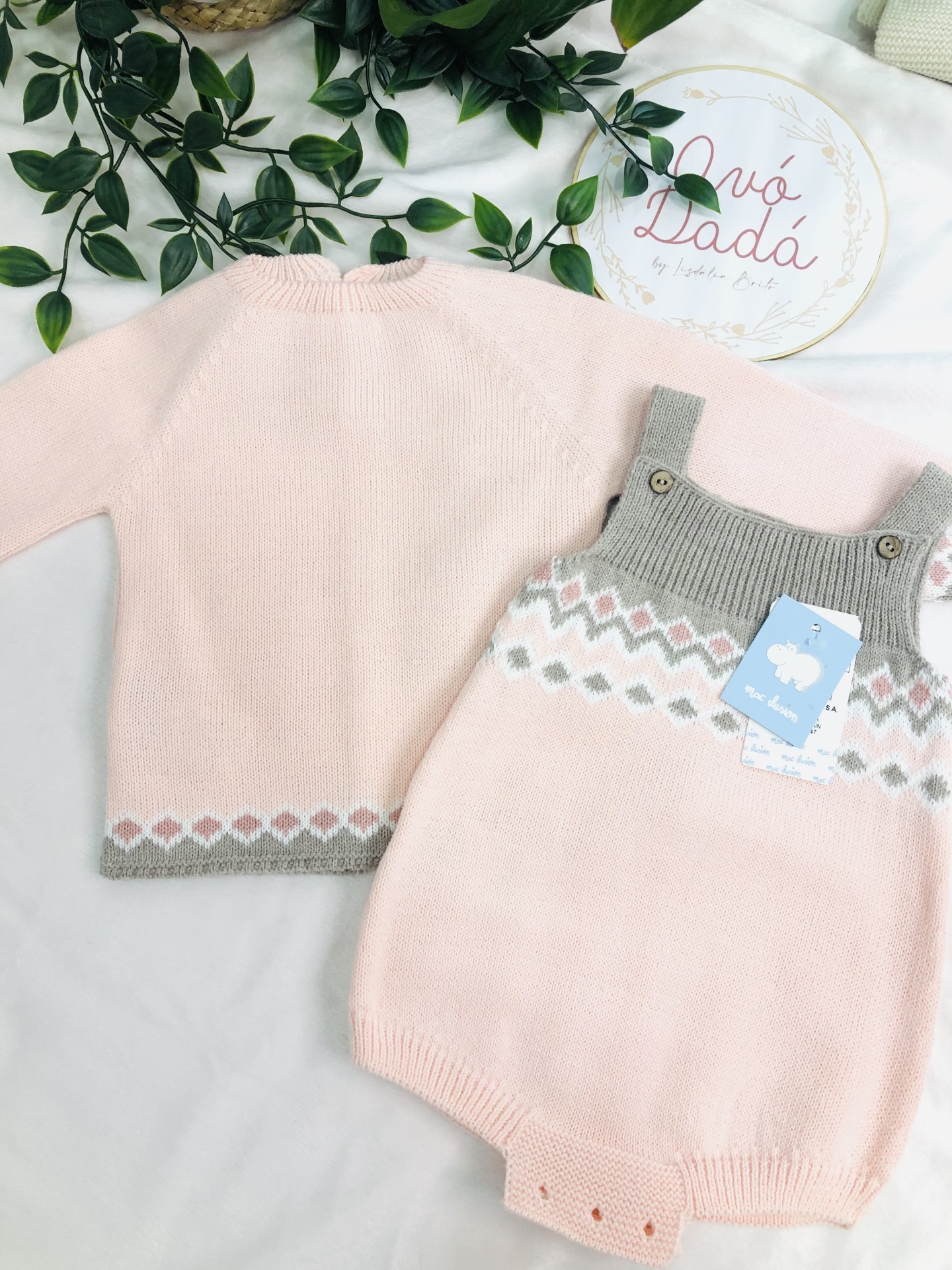 Conjunto de roupa de bebé em malha rosa e cinza com padrão geométrico e etiqueta azul