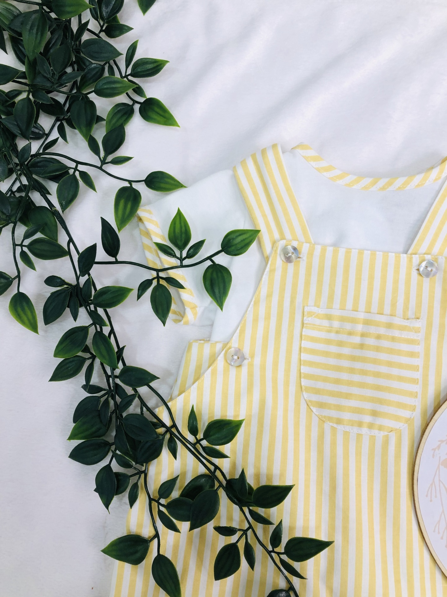 Macacão de bebé amarelo às riscas com t-shirt branca e planta verde