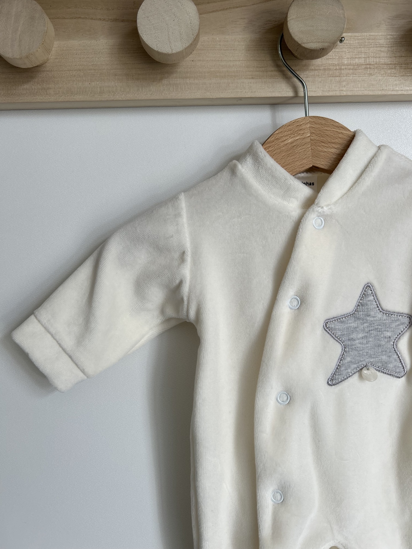 Roupa de bebé branca com estrela cinzenta pendurada em cabide de madeira