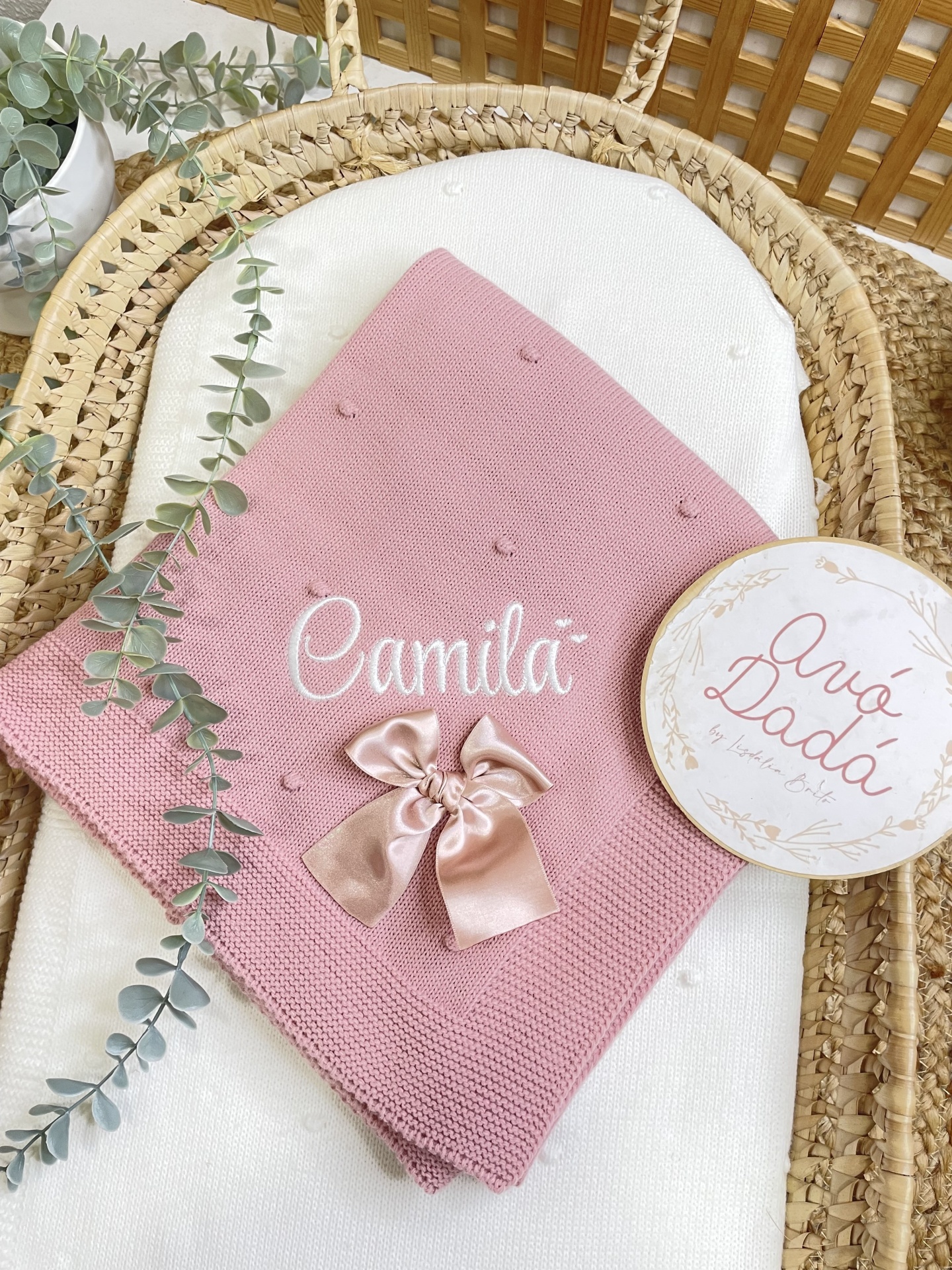 Cobertor bebé cor-de-rosa em malha com laço e bordado em suporte de vime com planta e cartão.