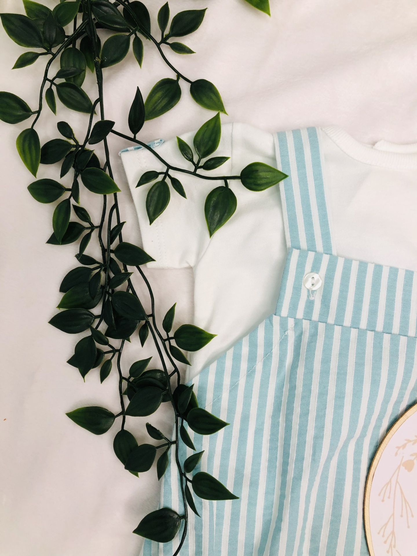 Conjunto de roupa para bebé branco e azul claro com folha verde ao lado