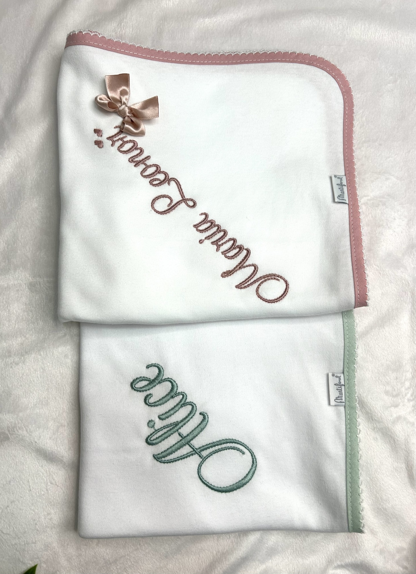 Dois panos de prato brancos com bordas coloridas e textos bordados, um rosa e outro verde