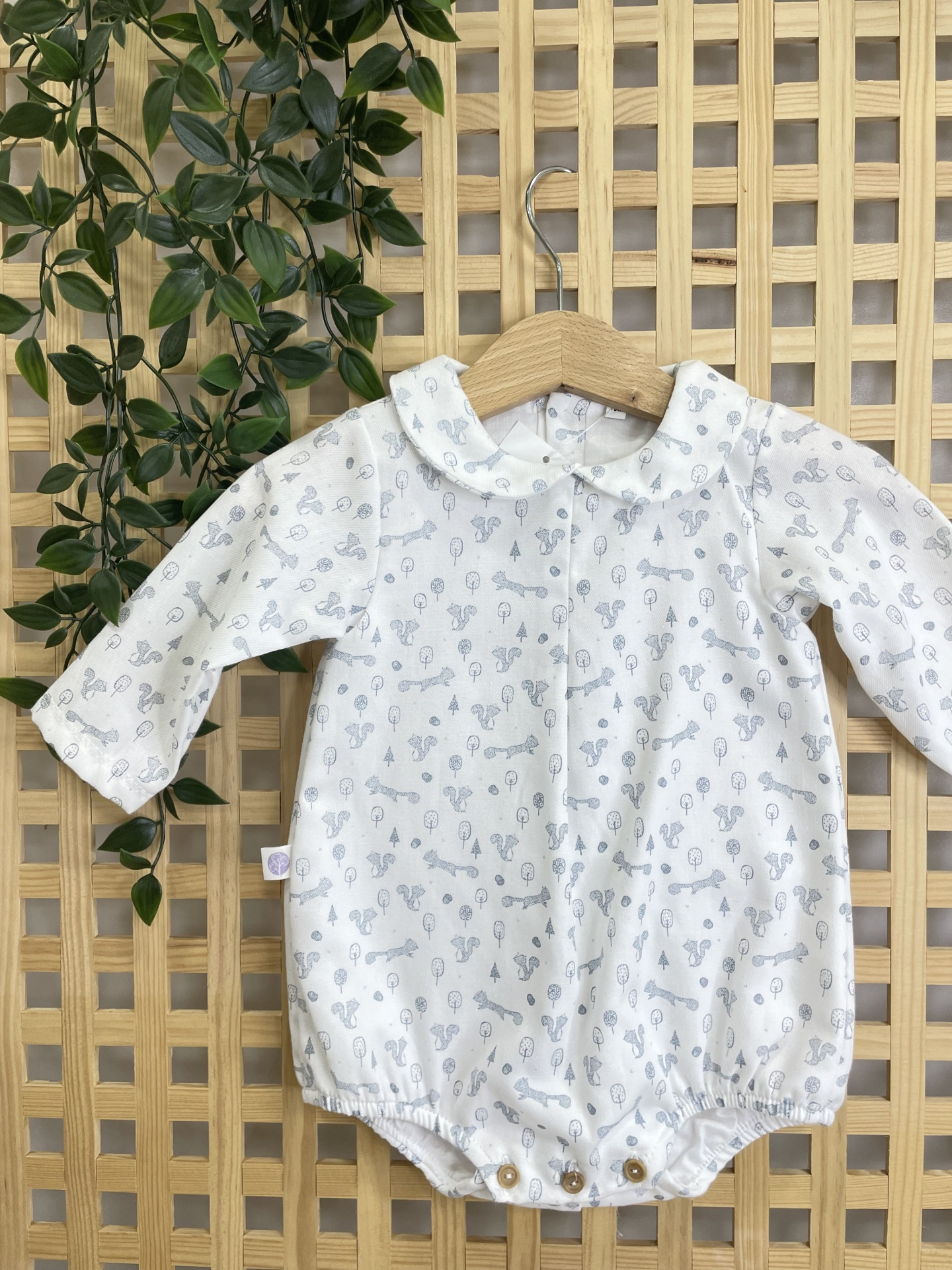 Body de bebé branco com padrão cinzento, com gola e botões, pendurado num cabide de madeira