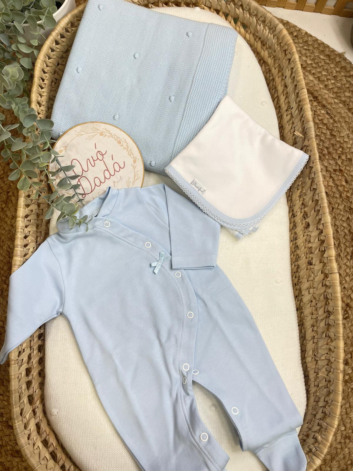 Conjunto de bebé azul claro com babygrow, manta e fralda numa cesta de vime