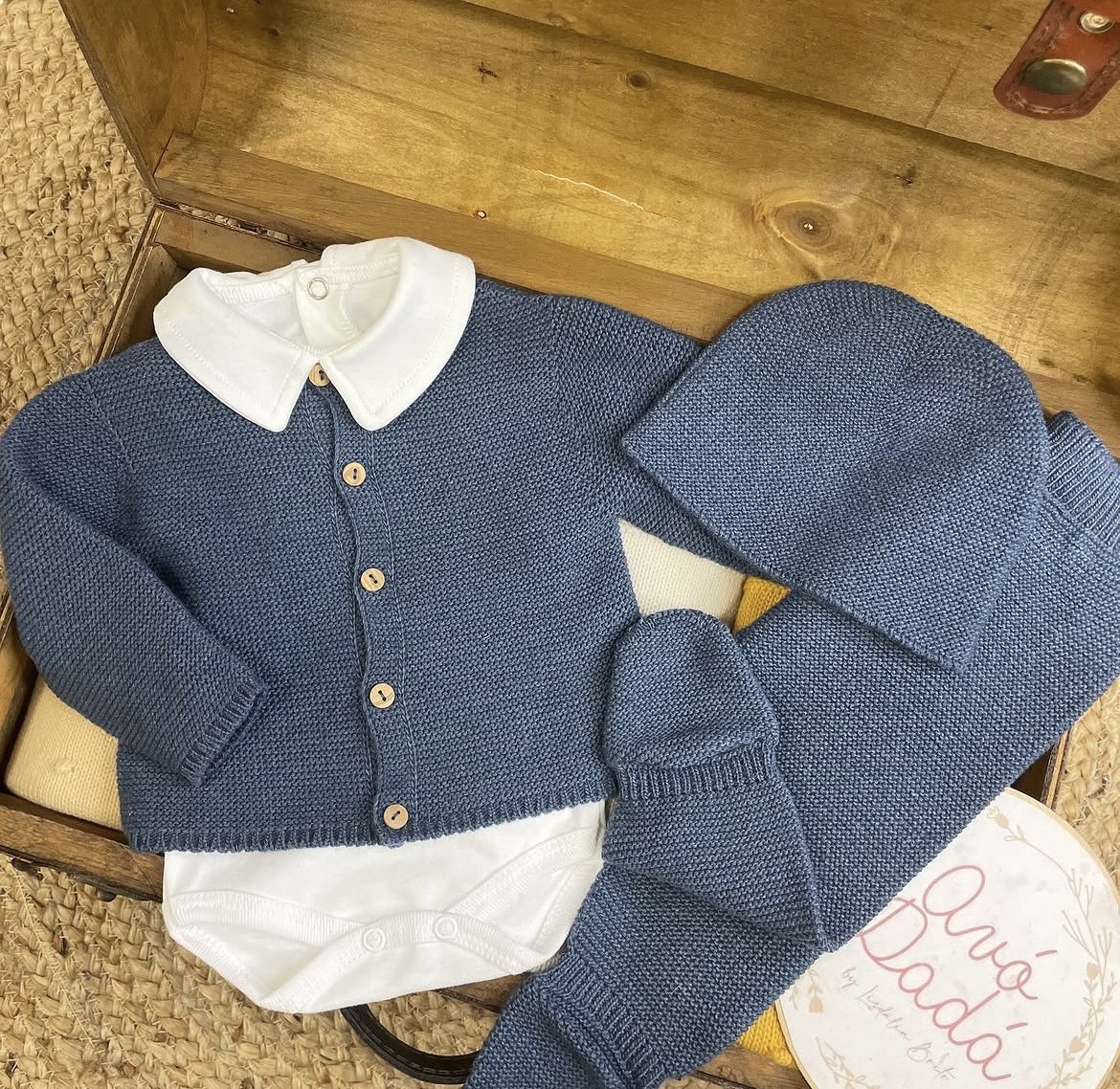 Conjunto de roupa de bebé azul com body branco e acessórios sobre mala de madeira