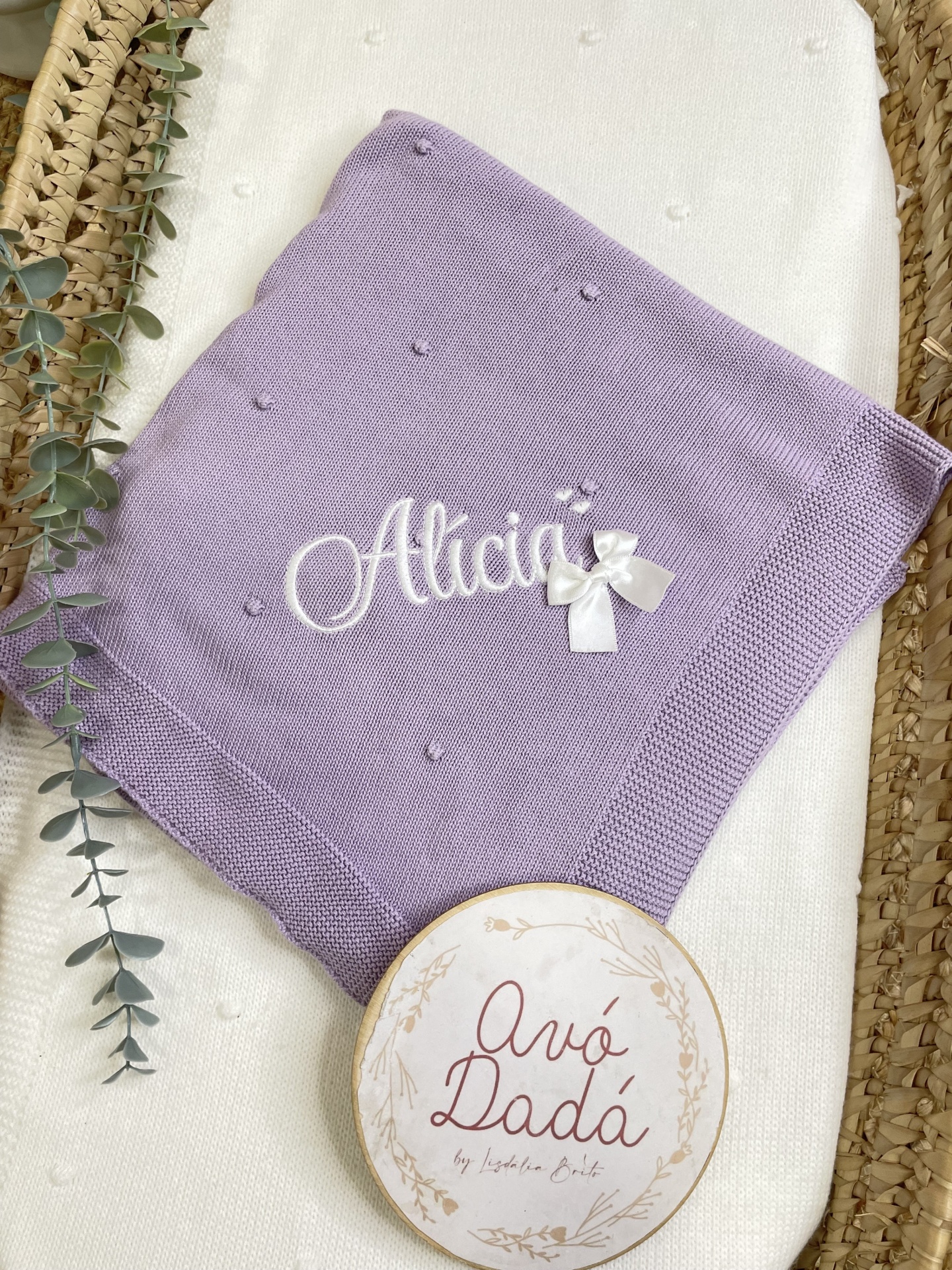Manta de bebé lilás bordada com o nome Alicia e cesto com placa Avó Dadá