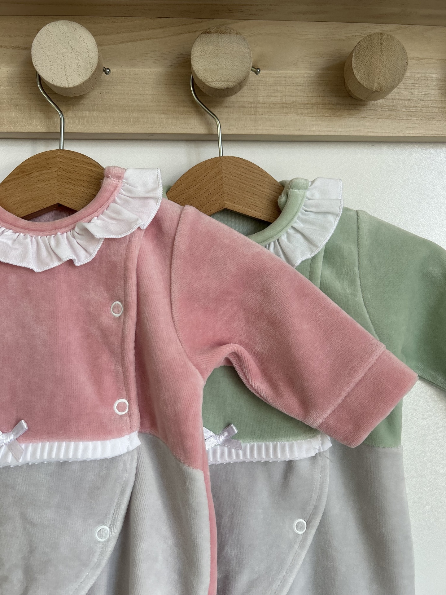 Dois macacões infantis em veludo rosa e verde com gola branca na parede