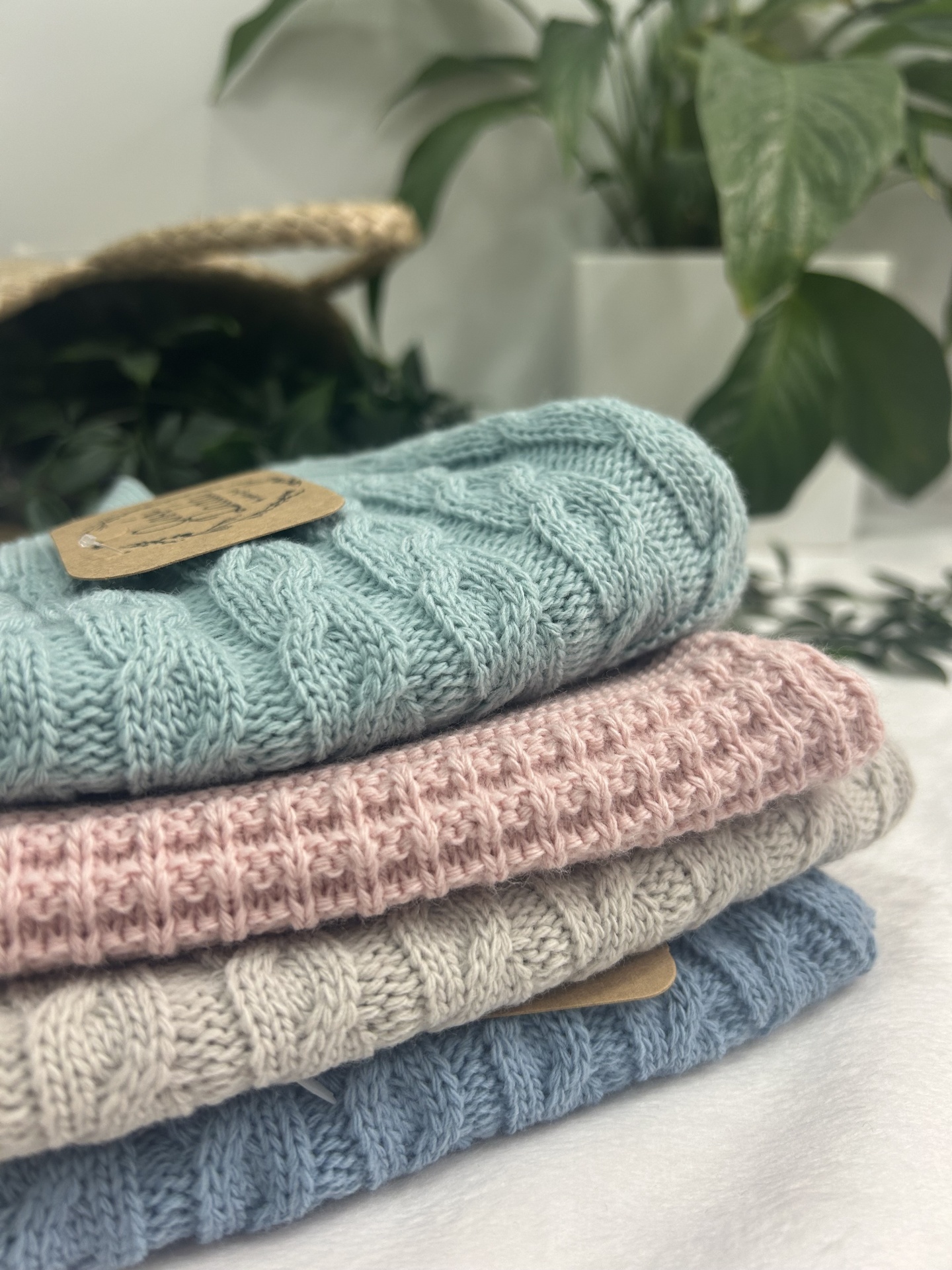 Conjunto de quatro peças de malha colorida dobradas com padrão trançado e ponto de malha, plantas ao fundo