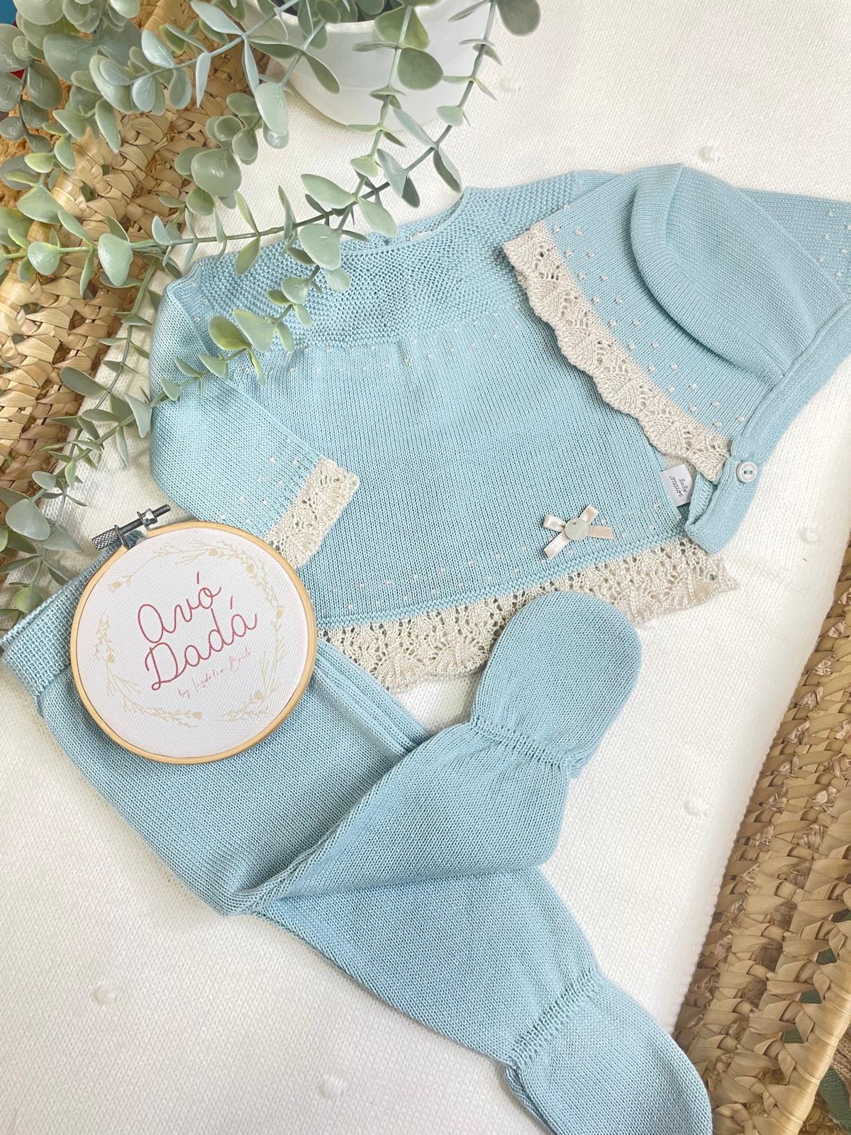 Conjunto azul de bebé com rendas bege e laço, gorro, camisola e calças.