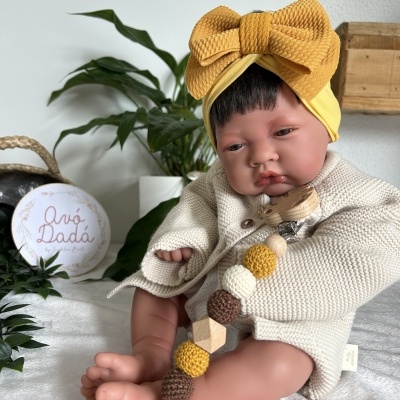 Boneca realista com camisola cremosa e faixa de cabeça amarela com laço