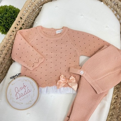 Conjunto de bebé rosa claro em malha com laço e saia branca sobre almofada branca em cesta de vime