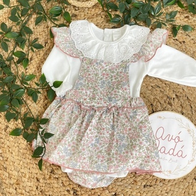 Conjunto de roupa para bebé com body branco e vestido floral rosa e verde sobre tapete natural