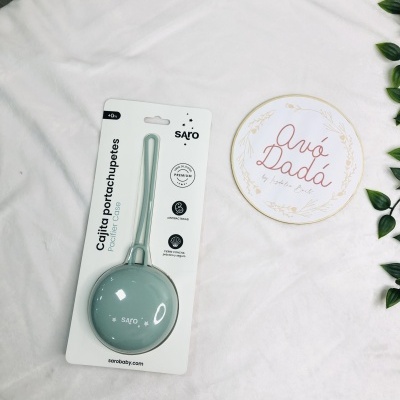 Estojo porta-chupetas verde claro em embalagem branca e placa redonda com texto Avó Dadá sobre tecido branco