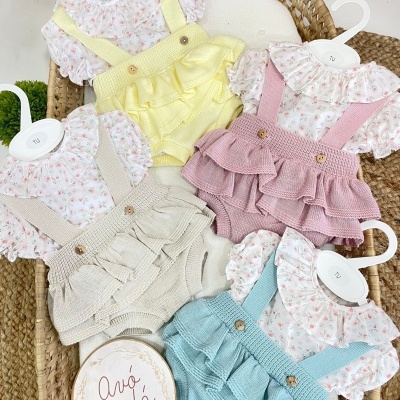 Conjunto de roupa para bebé com blusa floral e jardineira de malha colorida num berço de vime.