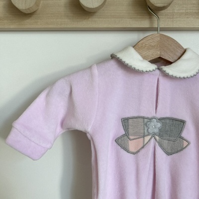 Macacão bebé rosa claro com gola branca e laço decorativo cinza e rosa, pendurado em cabide de madeira