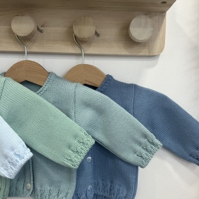 Três casacos de malha infantis pendurados em cabides de madeira