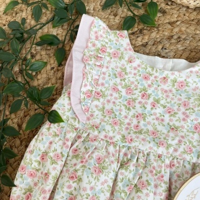 Vestido infantil floral branco com detalhes rosa sobre tapete de fibra natural