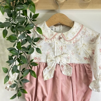 Body de bebé branco com padrão floral rosa e bege e parte inferior rosa claro pendurado em cabide de madeira