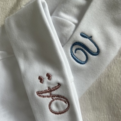 Tecido branco com bordados em azul e cor de rosa sobre uma superfície peluda clara