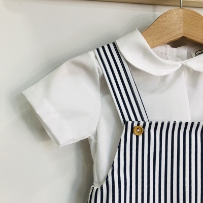 Roupa de bebé branca com macacão riscado azul e branco pendurada num cabide de madeira