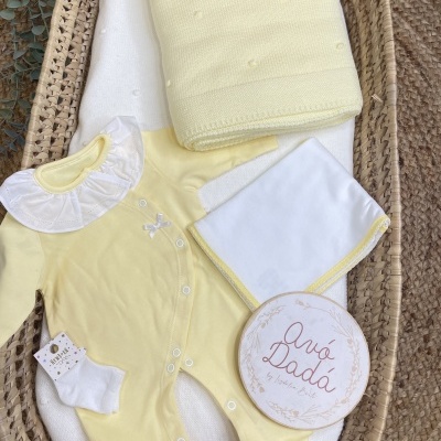 Conjunto de roupa de bebé amarelo com colarinho branco, meias, manta amarela e cesto de palha
