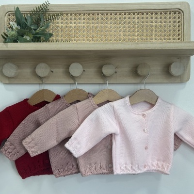 Conjunto de casacos de malha para bebé pendurados numa prateleira de madeira com vime e planta decorativa