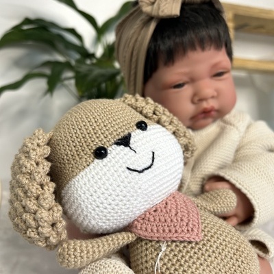 Bebé com boneco cão em crochet beige sentado, com planta verde e prateleira de madeira