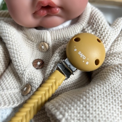 Chupeta amarela com clip e cordão sobre roupa creme de boneca realista