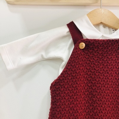 Roupa de bebé com vestido vermelho de malha e camisa branca pendurada num cabide de madeira